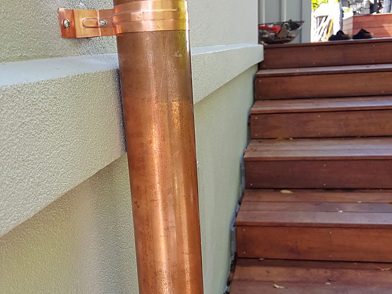 Copper downpipe installed against a plastered wall